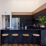 A photo of a kitchen with four chairs, plants, a fridge and a painting on the wall.