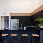 A photo of a kitchen, with 4 chairs, a plant, a fridge and a red paining on the wall.