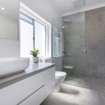 A photo of a bathroom with a sink, a plant next to it, a toilet and a shower with a towel rack.