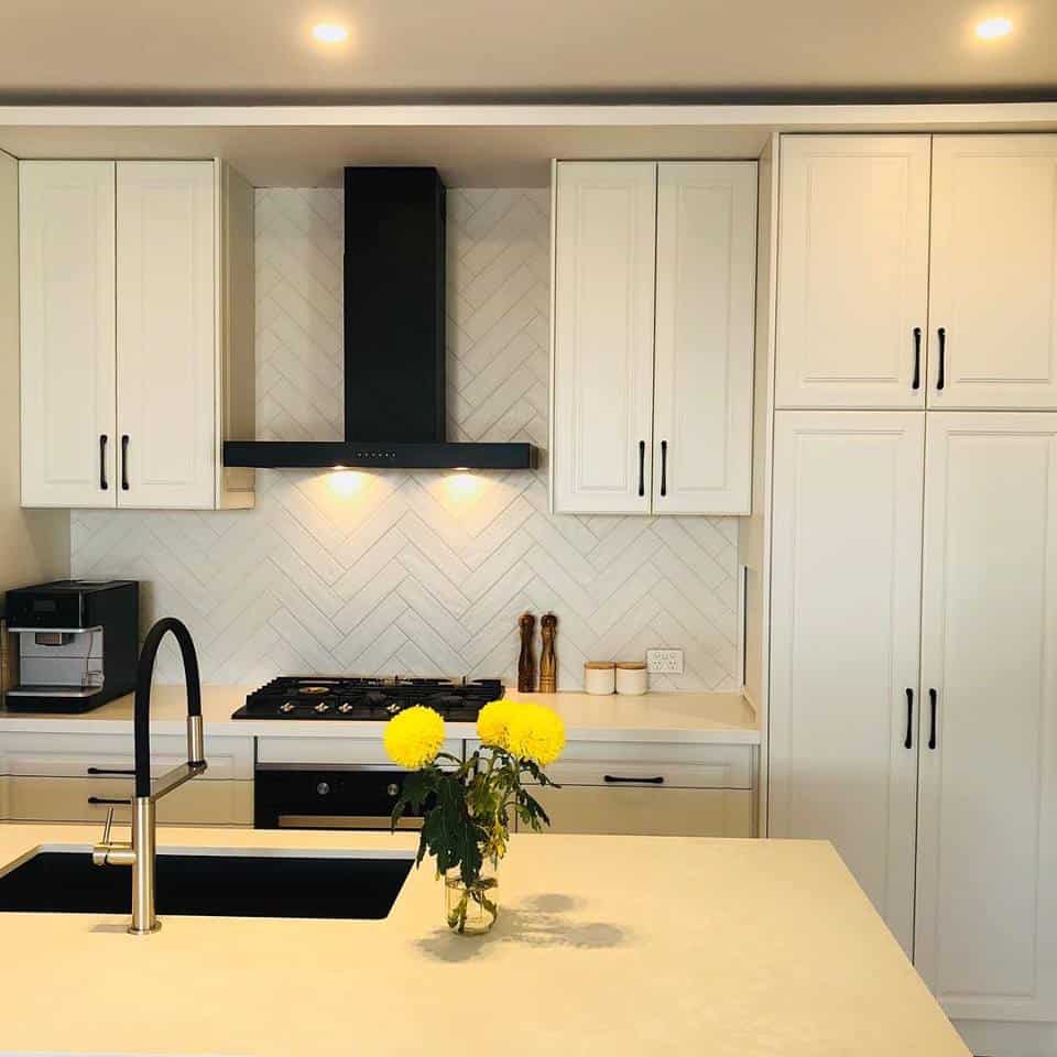 A photo of a kitchen area, with a stove, sink and vase with yellow flowers.