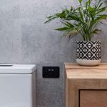 A photo of a toilet and side table, with a black wall socket between them.