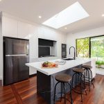 A photo of a kitchen area, with a centre island table, a large fridge and stove in the bacgkround.