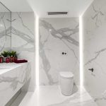 A photo of a bathroom area, with a large sink, toilet and wall lights emitting out behind the wall behind the toilet.