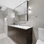 A photo of a large bathroom area, with a rectangular tap and large mirror, shower in the background.