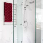 A photo of a towel rack, with a red towel on it. There is a shower behind it with glass doors.