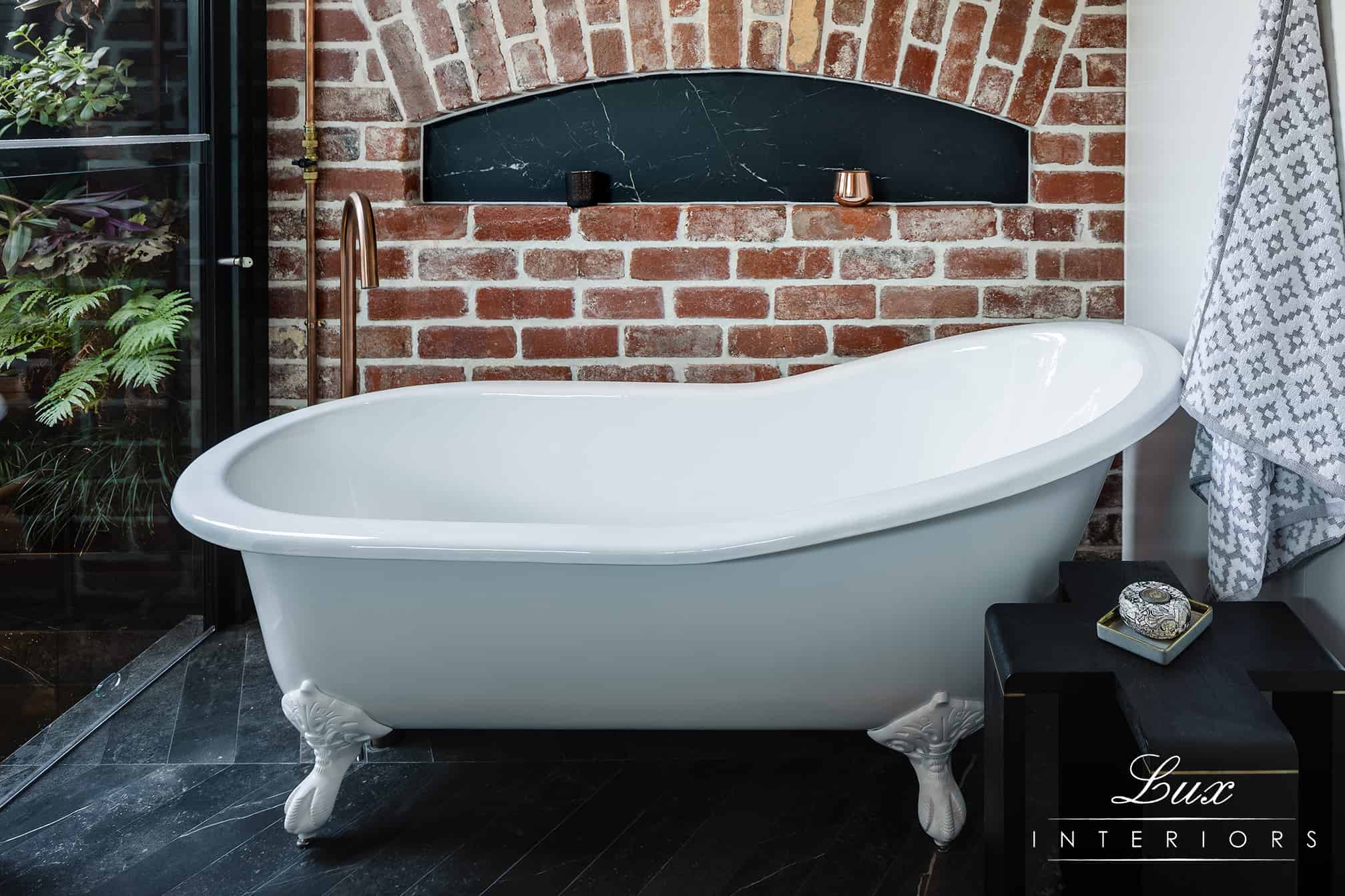 A photo of a bath tub, with a gold tap running into it, a wall of bricks behind the bath.