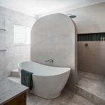 A photo of a curved dividing wall in a bathroom, in front of a bath tub.