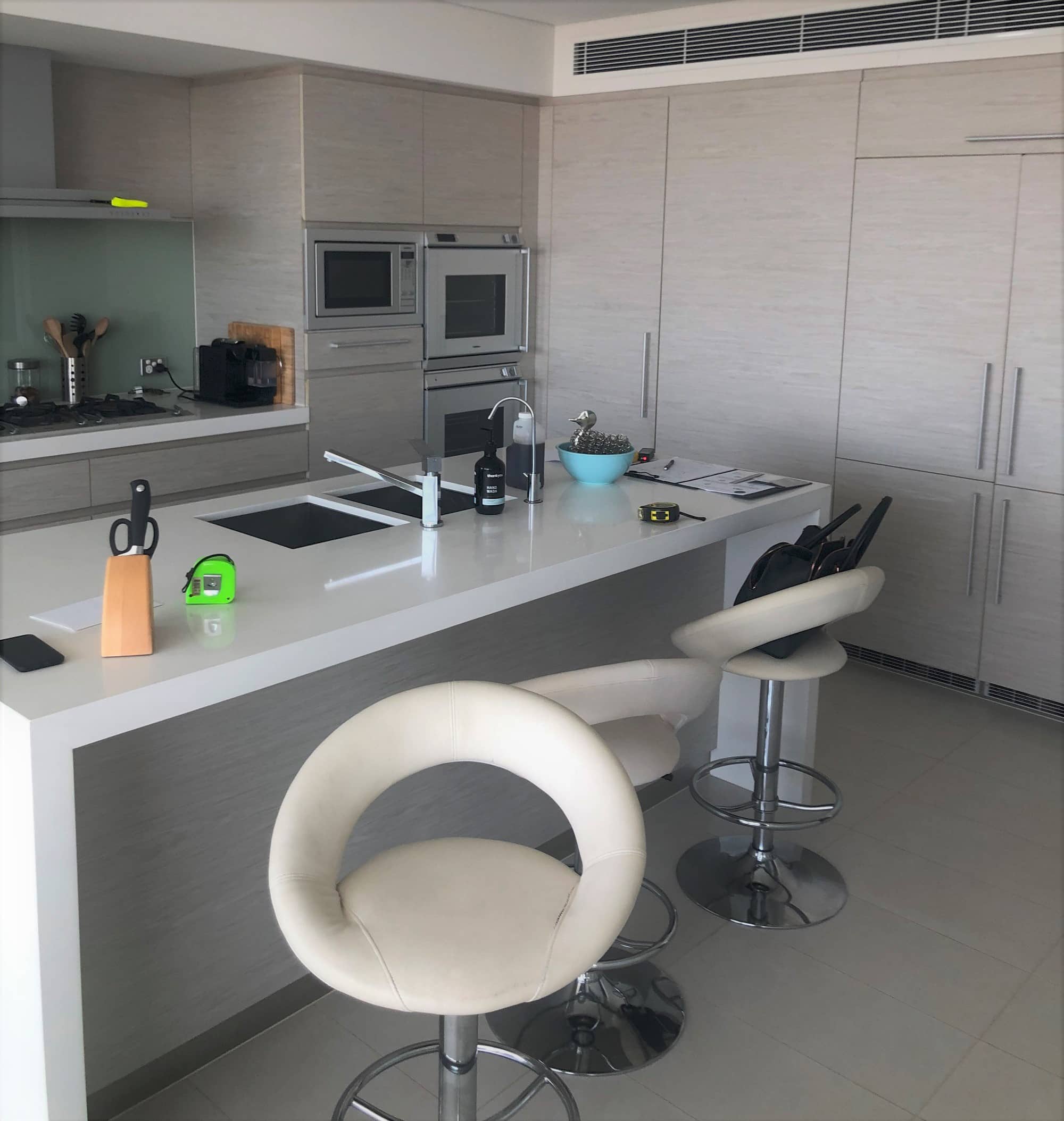 A photo of a kitchen area, with circular seats, white bench top and grey cabinets.