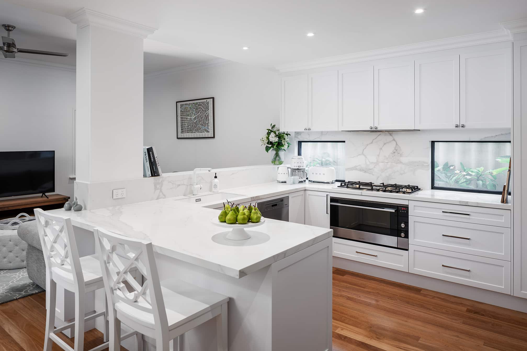 A photo of a kitchen area, all white with wooden floorboards.