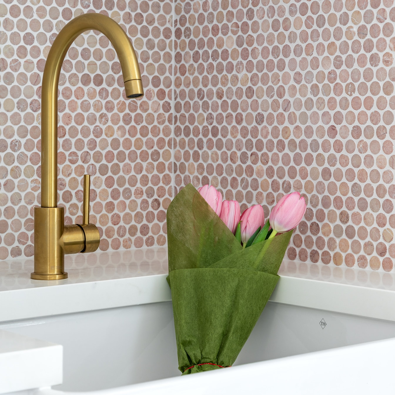 A photo of a laundry sink. There are flowers in the sink. The tap is gold.