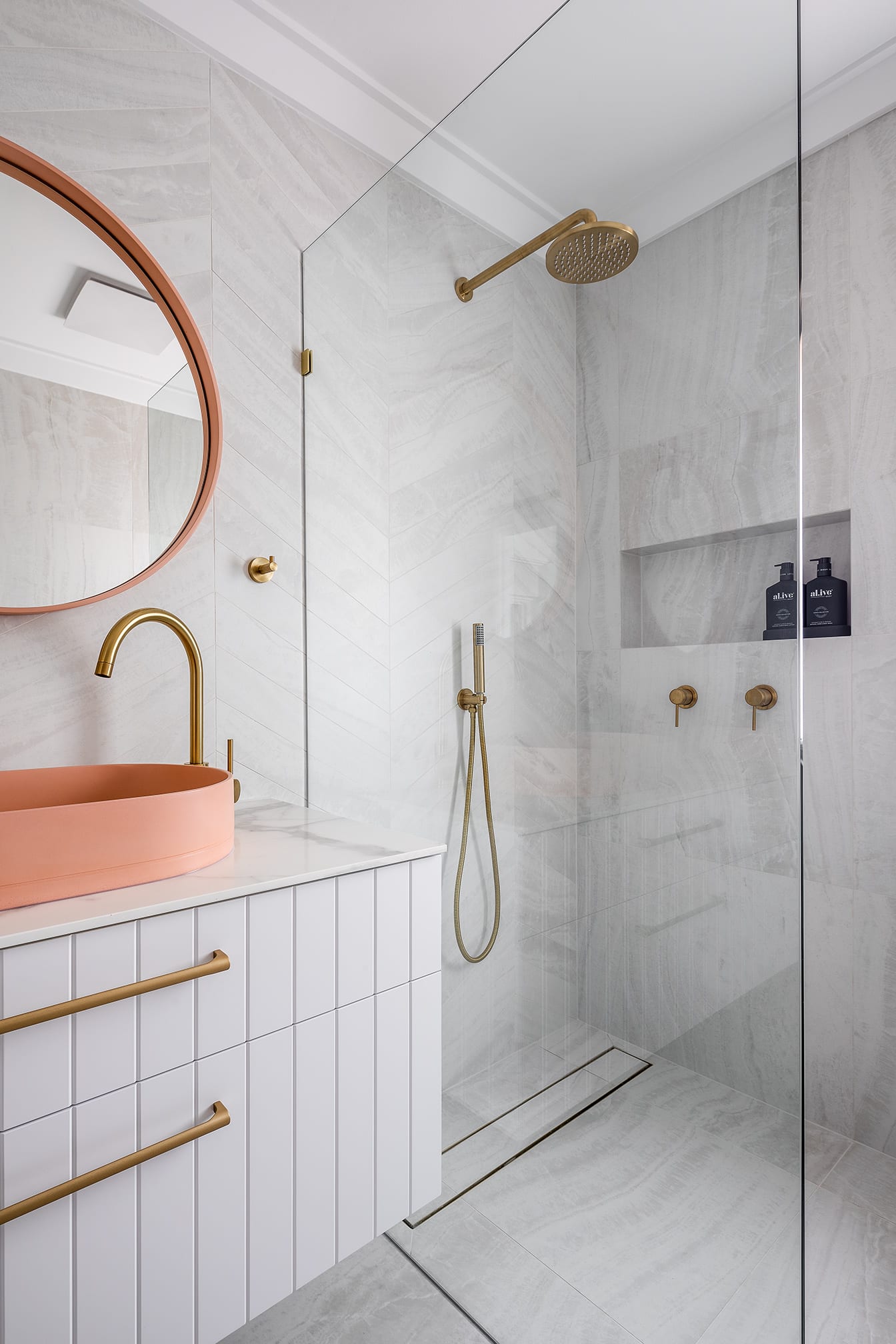 A photo of an open shower area next to a sink and round mirror.