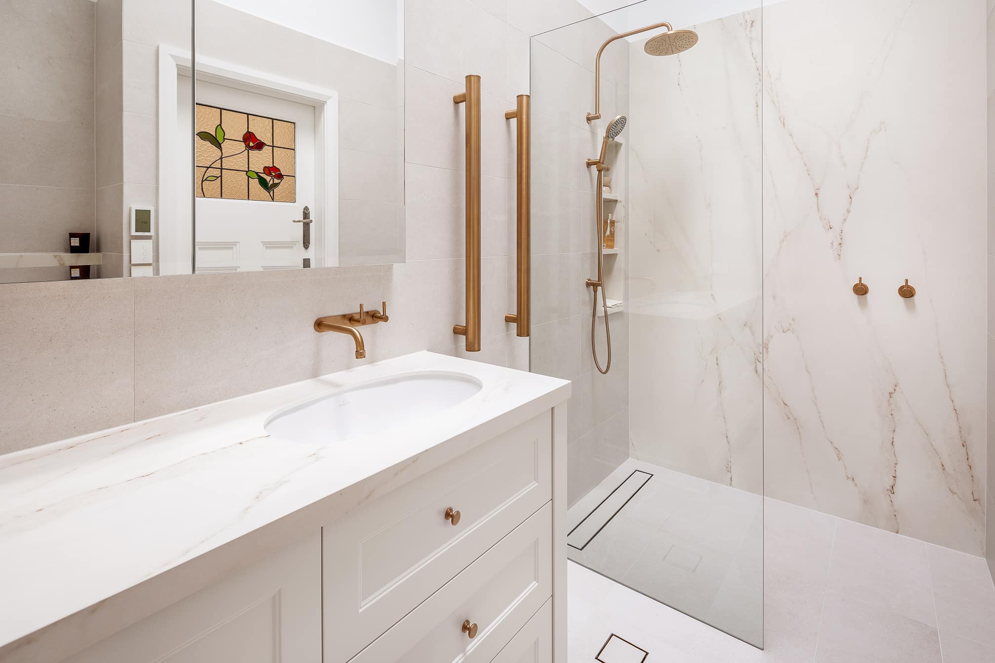 A photo of a freshly renovated bathroom, with gold tapware and a glass shower.