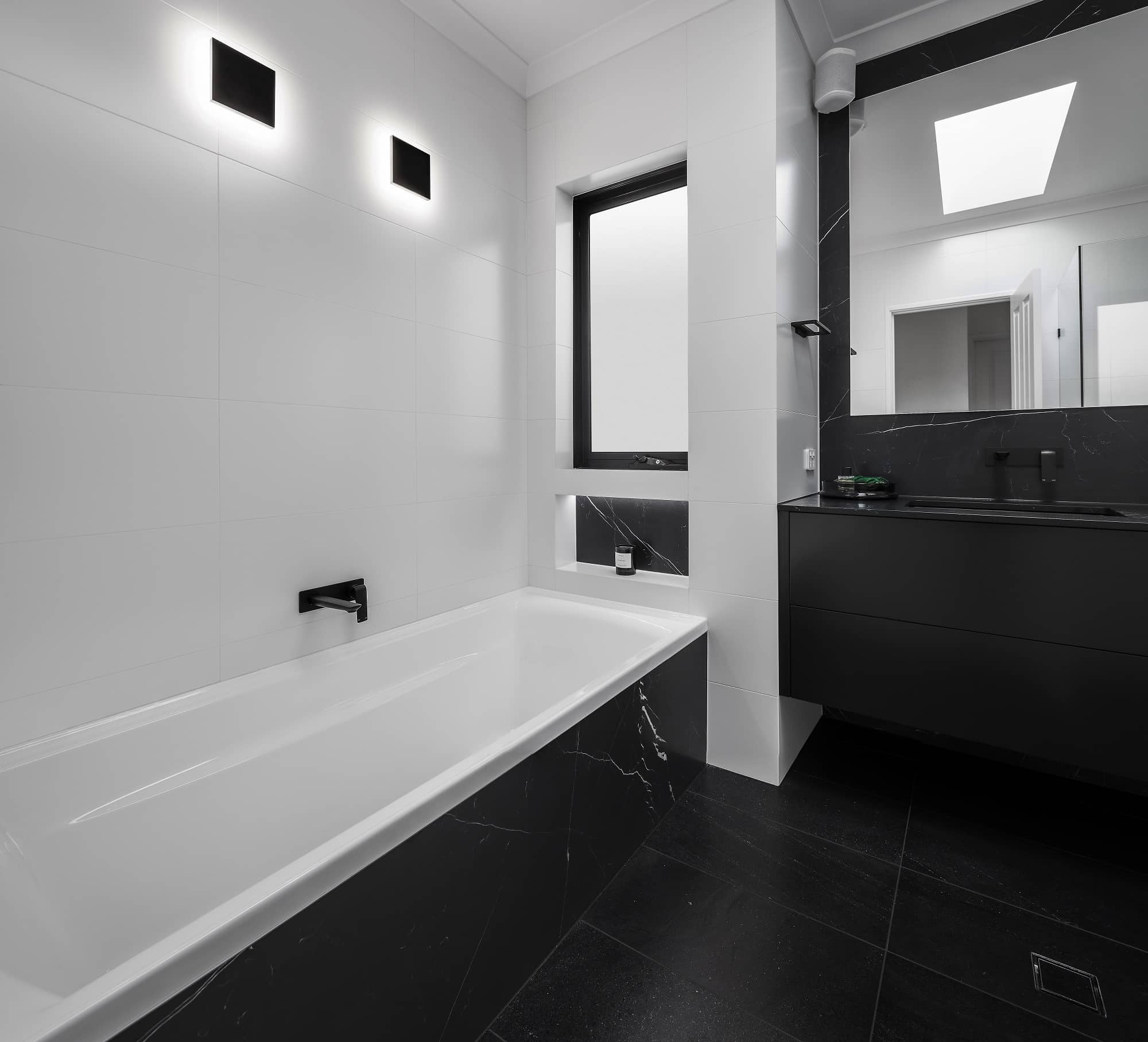 A photo of a bathroom, with a bath tub in the corner, sink and bluetooth speaker in the top corner of the sink.