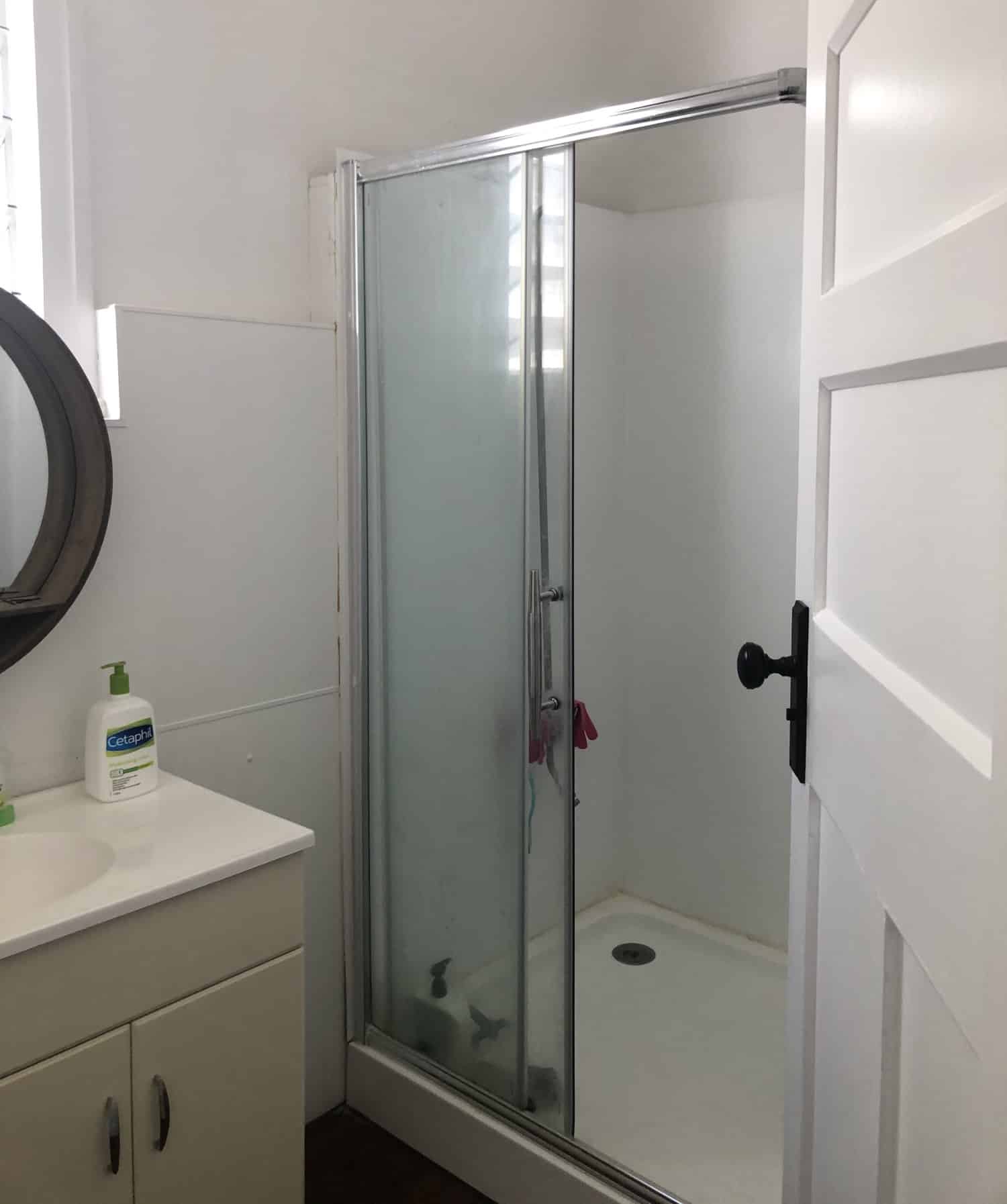 A photo of a bathroom area, before being renovated by Lux Interiors. There is a shower and sink and looks old and uninviting.