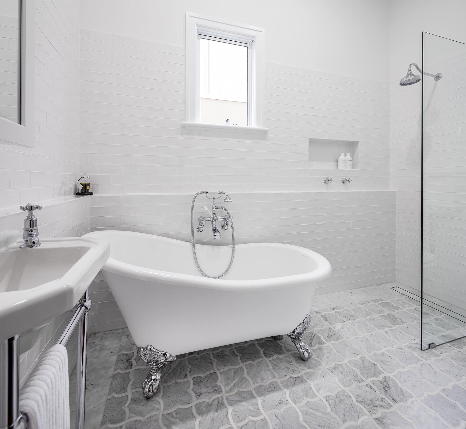 A photo of a newly renovated bathroom area, with white walls, white bath and glass shower.