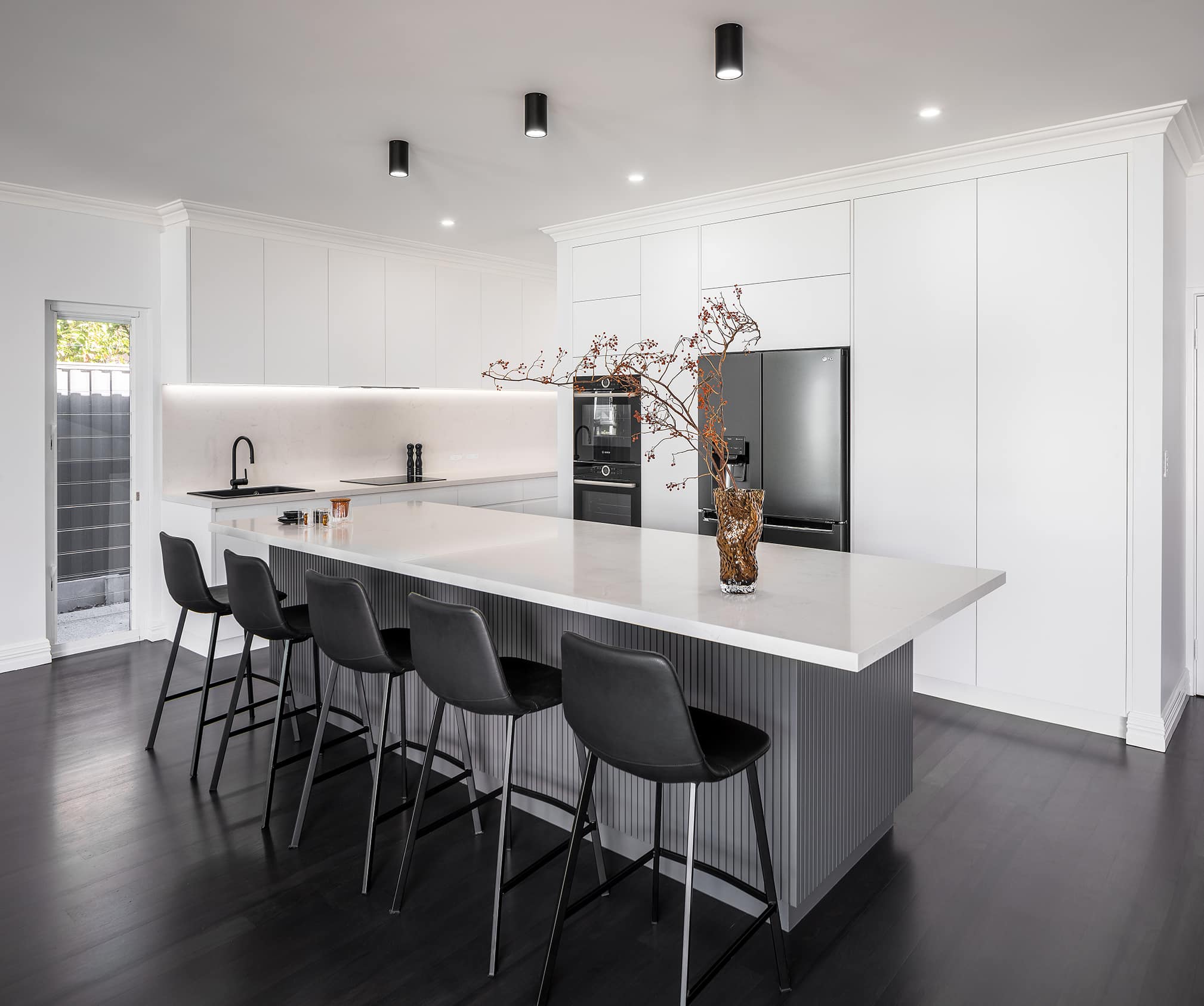 A photo of a newly renovated kitchen, mostly white, with black floorboards and gold decorations.