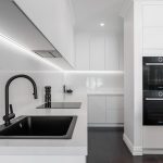 A photo of a kitchen area, with sink, stove and two ovens.