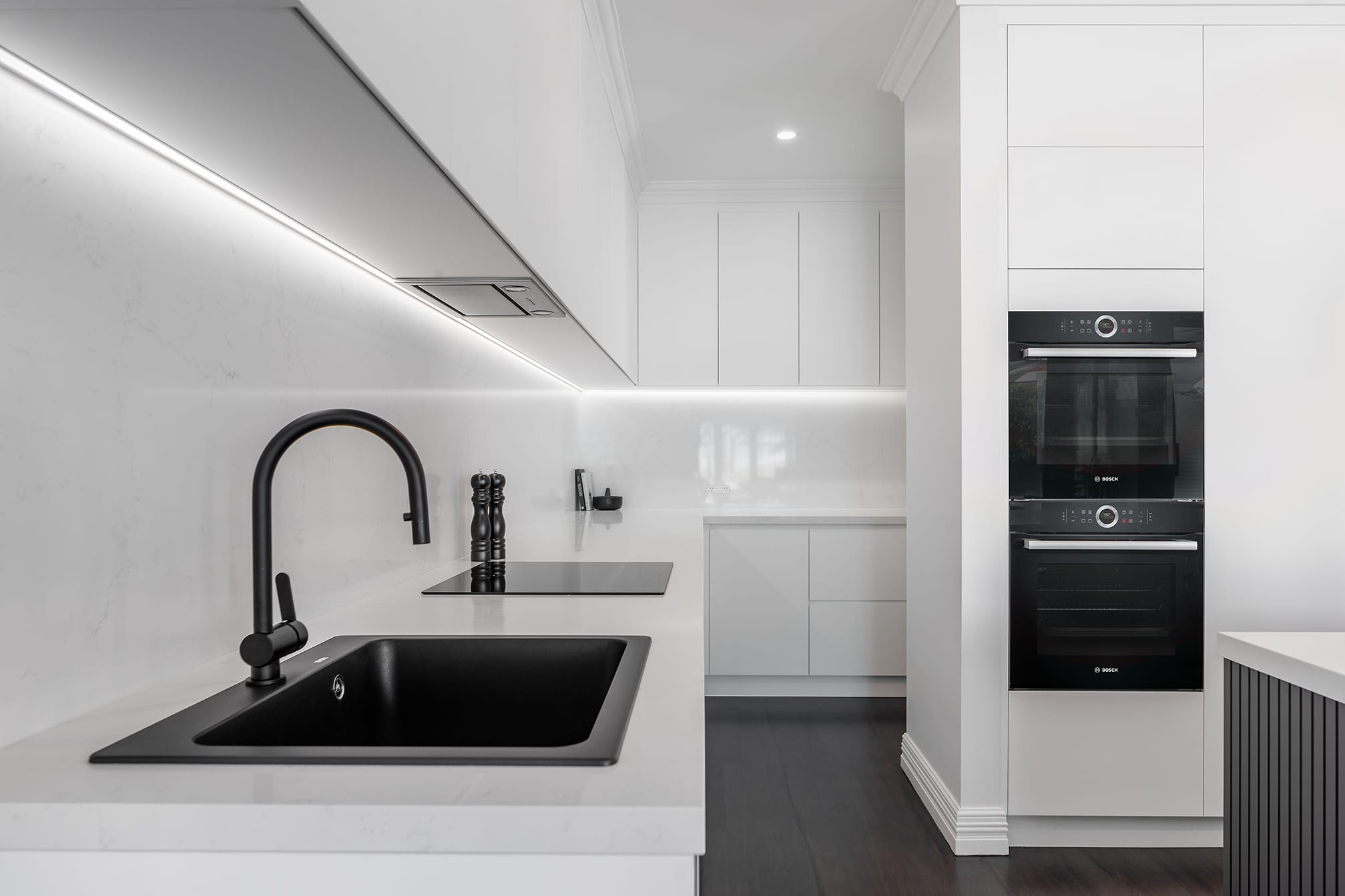 A photo of a kitchen area, with sink, stove and two ovens.