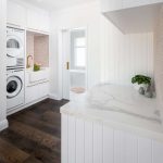 A photo of a North Beach coastal barn laundry renovation with brass, white v groove panelling and pink penny round tiles. There is a washing machine and dryer in the background.