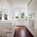 Renovated white kitchen with wooden floor and marble countertop.