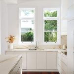 White kitchen with wooden floor and tree outside of window