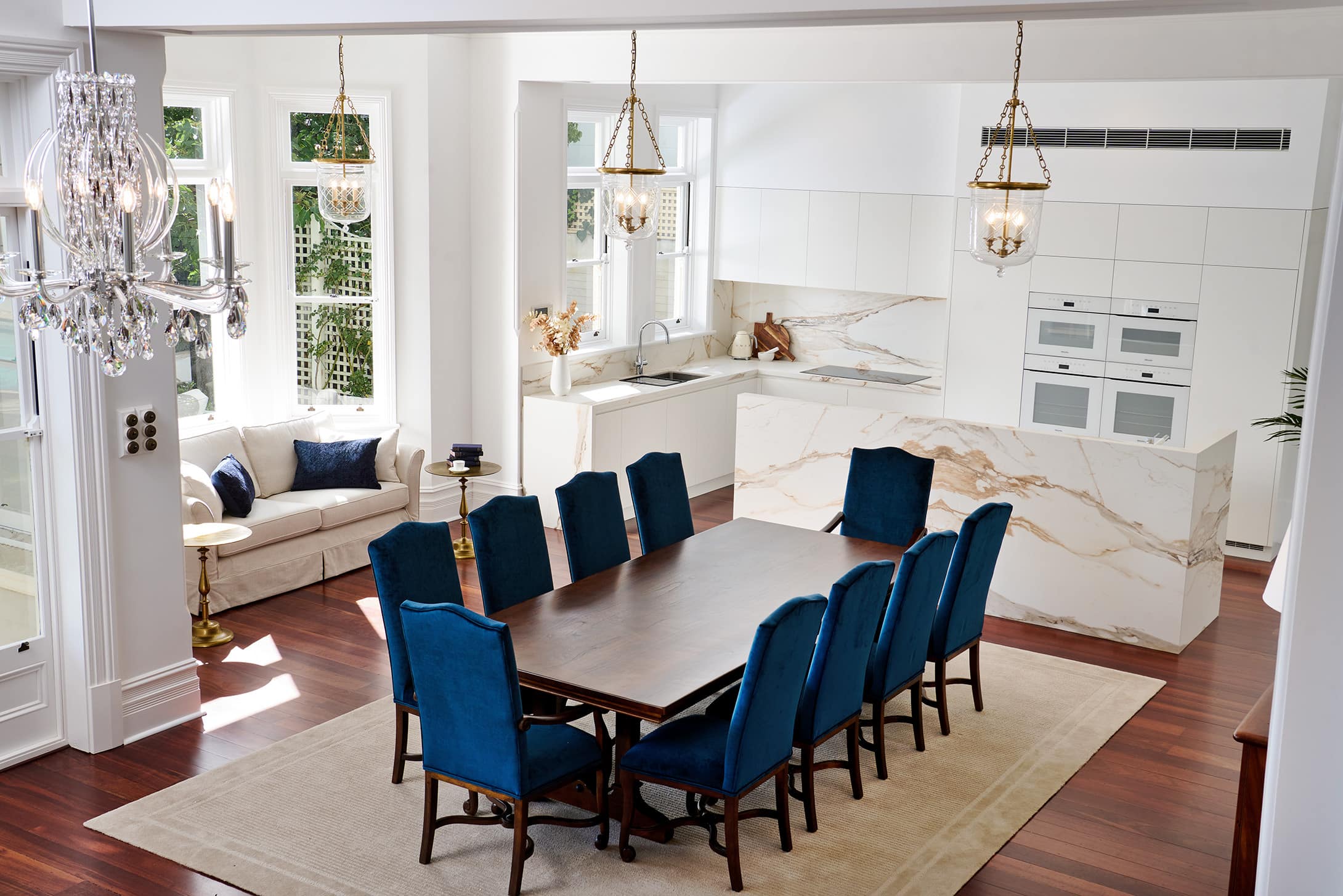 A photo of a fully renovated kitchen area with white marble decorations paired with royal blue chairs and pillows on the couches.