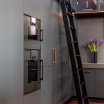 A photo of an industrial style kitchen renovation with black cabinetry and rolling library ladder.