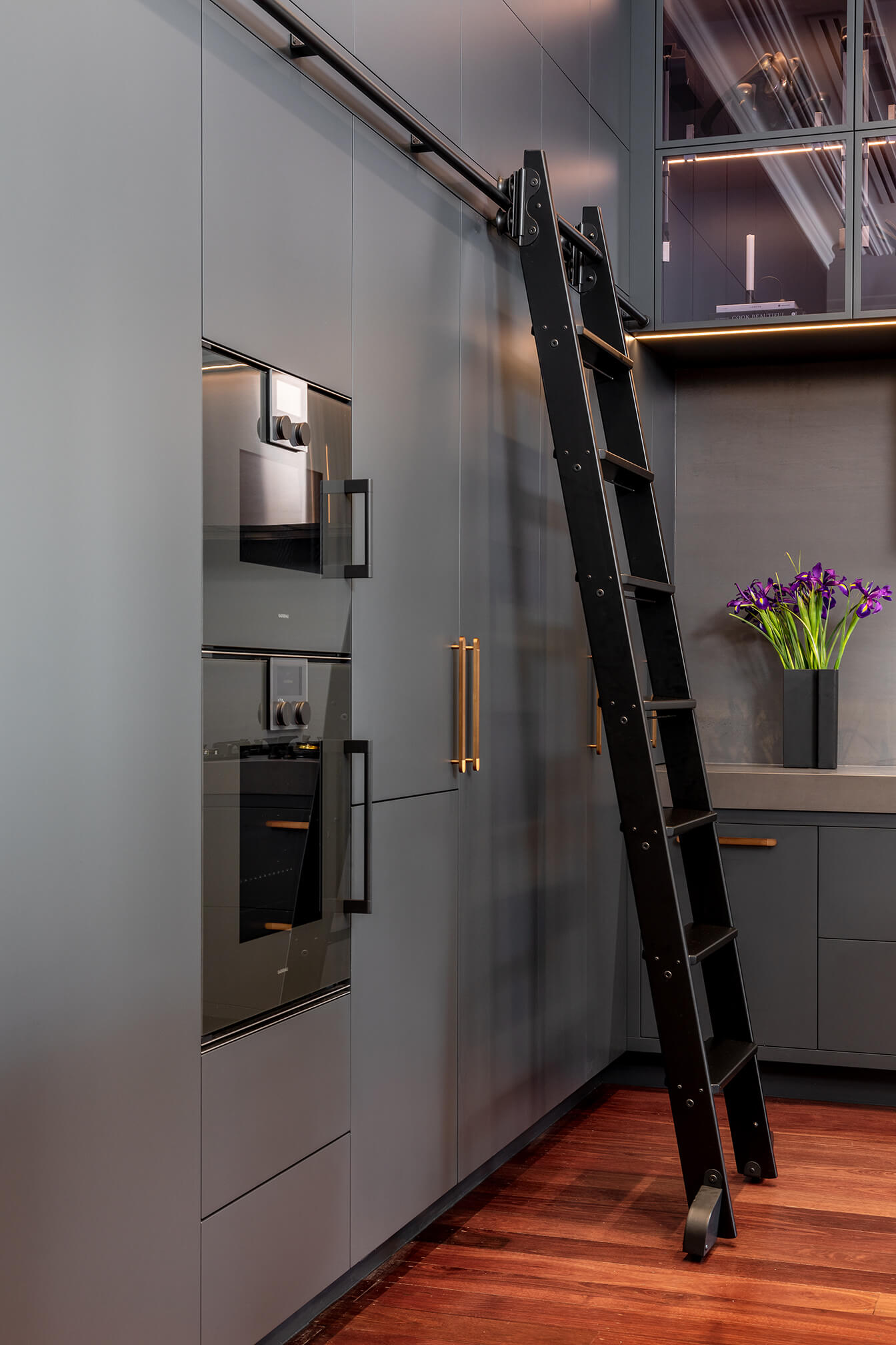 A photo of an industrial style kitchen renovation with black cabinetry and rolling library ladder.