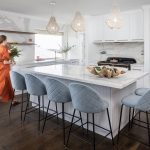 A photo of a centre island table, in a kitchen, with a woman walking to the side, wearing an orange dress.