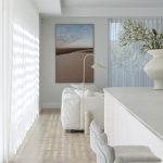 A photo of a living area, next to the kitchen. There is a variety of white furniture including a couch, high chairs and table.