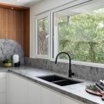 A photo of a kitchen sink, in front of a window. There are some books next to the sink.