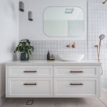 A photo of a bathroom sink, with draws and rounded mirror. There is a shower next to the sink.