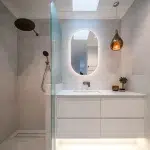 A photo of a bathroom, with a shower, sink and rounded mirror.