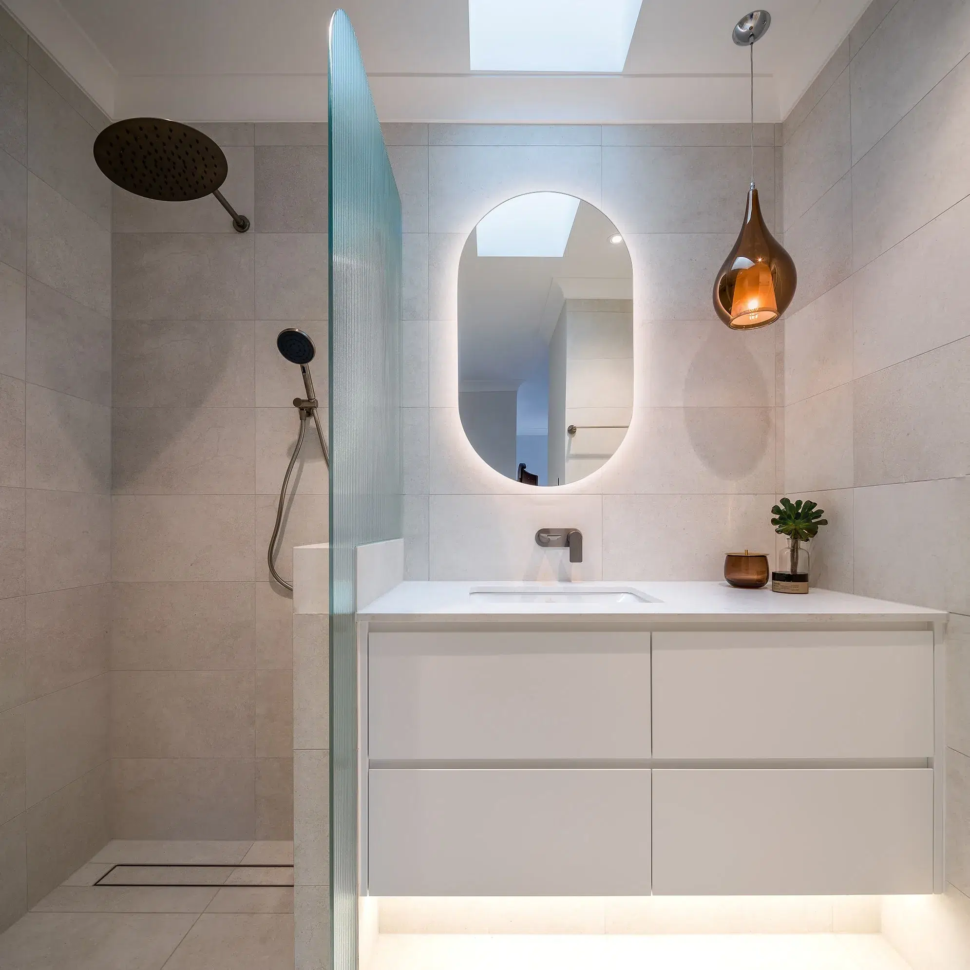 A photo of a bathroom, with a shower, sink and rounded mirror.