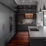 A photo of a kitchen area, all black, with polished wood floors.