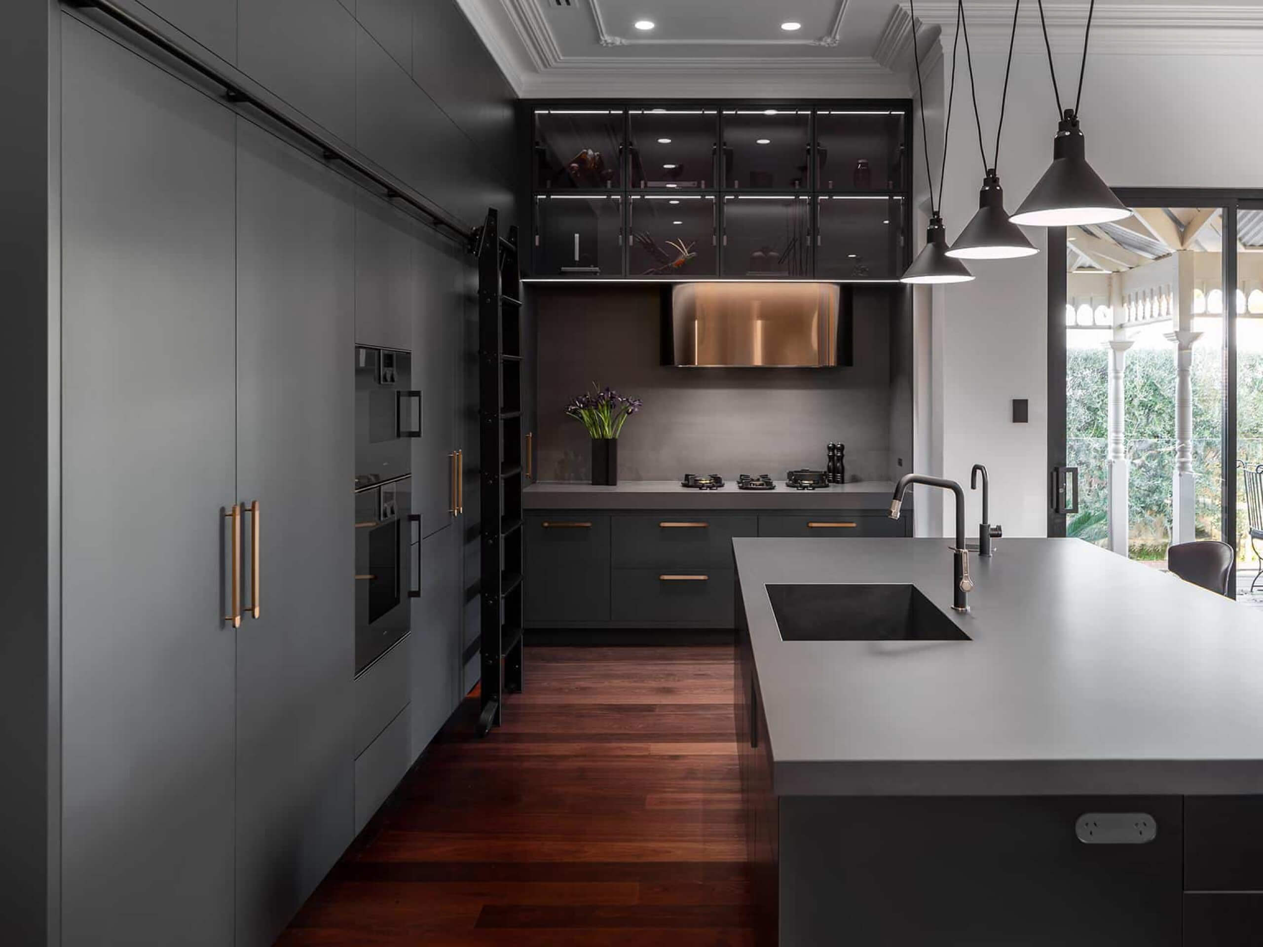 A photo of a kitchen area, all black, with polished wood floors.