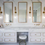 A photo of a bathroom with dual sinks, and imperial feeling mirrors and lights.