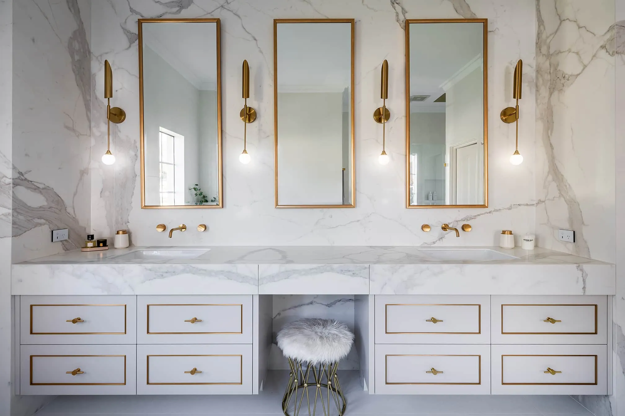 A photo of a bathroom with dual sinks, and imperial feeling mirrors and lights.