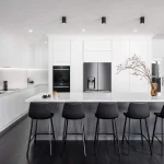 A photo of a kitchen, with black floors, white tables and black chairs.