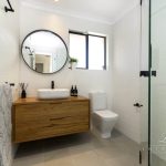 A photo of a bathroom, with a circle mirror, sink and shower.