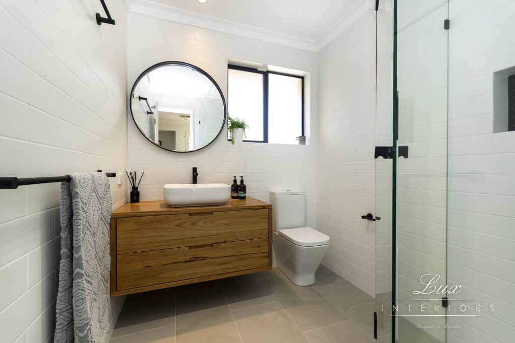 A photo of a bathroom, with a circle mirror, sink and shower.