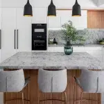 A photo of a kitchen, with white cabinets, marble grey table and tabletops.