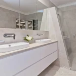 A photo of a bathroom with dual sinks, large mirror and shower.