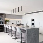 A photo of a kitchen, with a granite grey table, kitchen sink and bar.