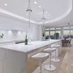 A photo of a white kitchen, with a stone kitchen island table, chairs and a bottle of champagne on the table.