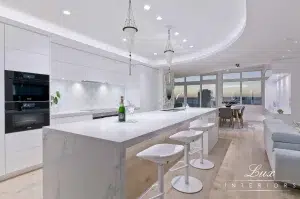 A photo of a white kitchen, with a stone kitchen island table, chairs and a bottle of champagne on the table.