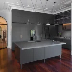 A photo of a kitchen, all black, with a kitchen island table and cabinets in the background.