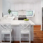 A photo of a kitchen, with an L shaped kitchen island, black fridge and stovetop.