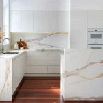 A photo of a kitchen, with stone bench-tops and a gold look & feel.