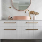 A photo of a single sink, with a round mirror above it, and a bath tub to the side.